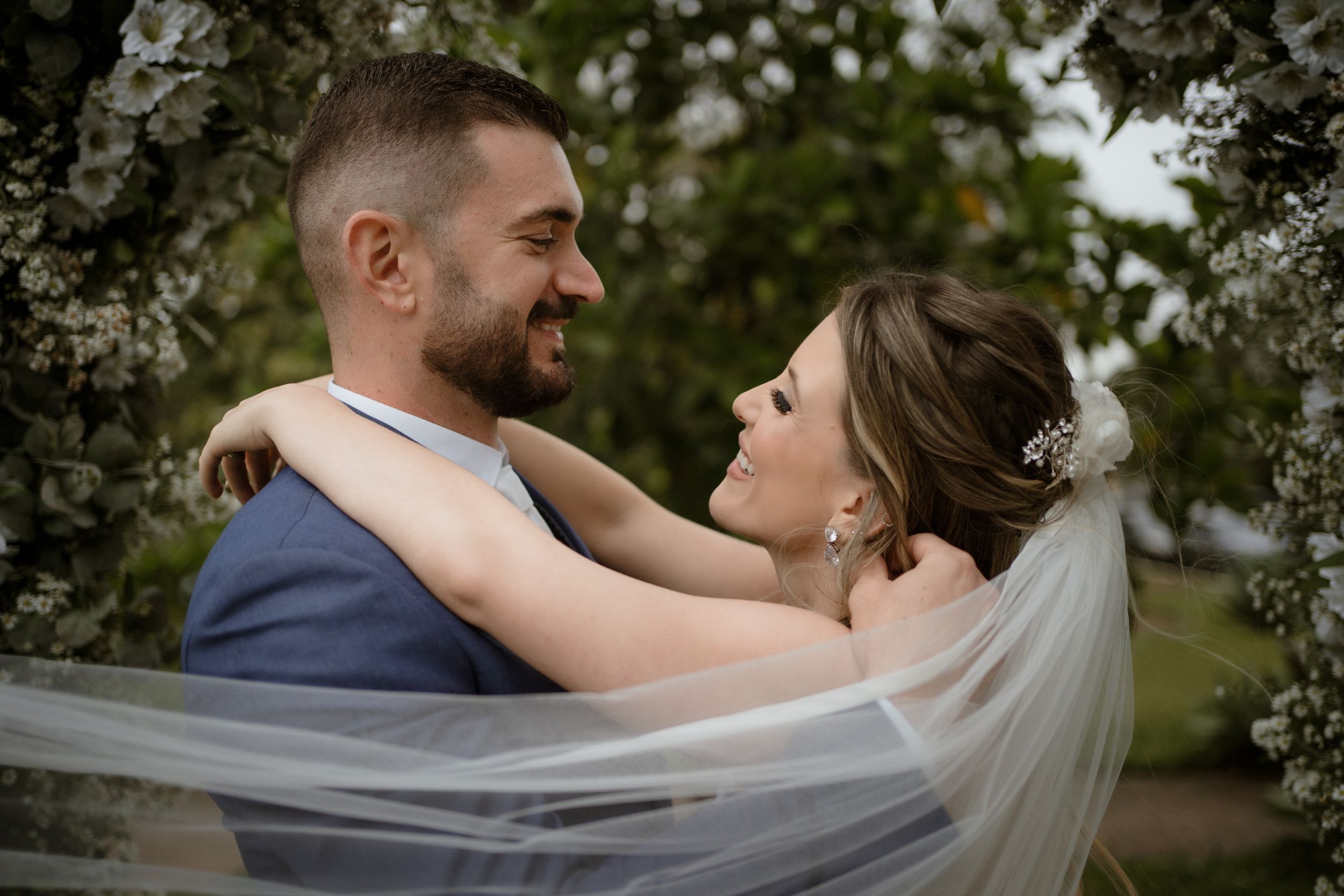 Romantic couple embracing under flowing veil surrounded by blooming spring flowers.
