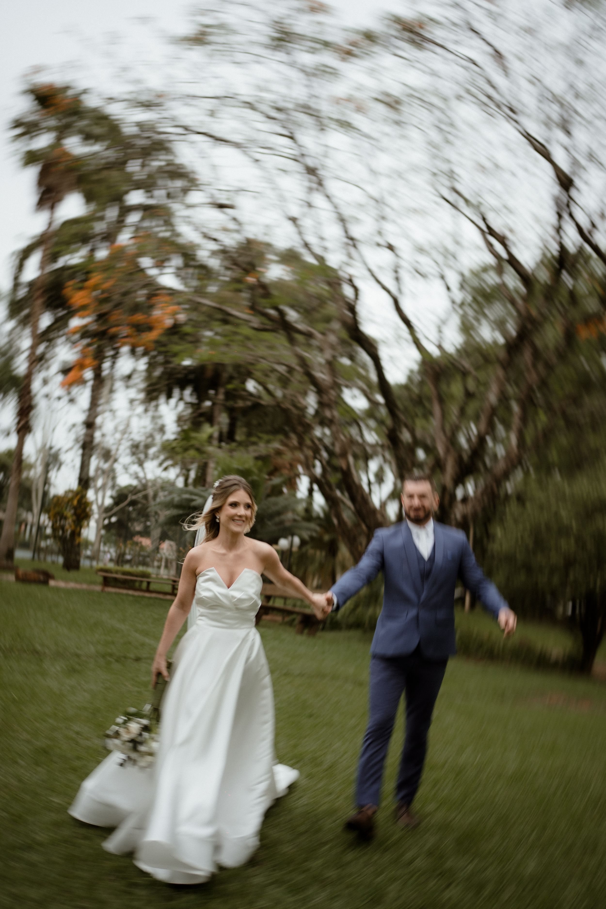 Dynamic motion shot of newlyweds running through a garden with trees in the background.