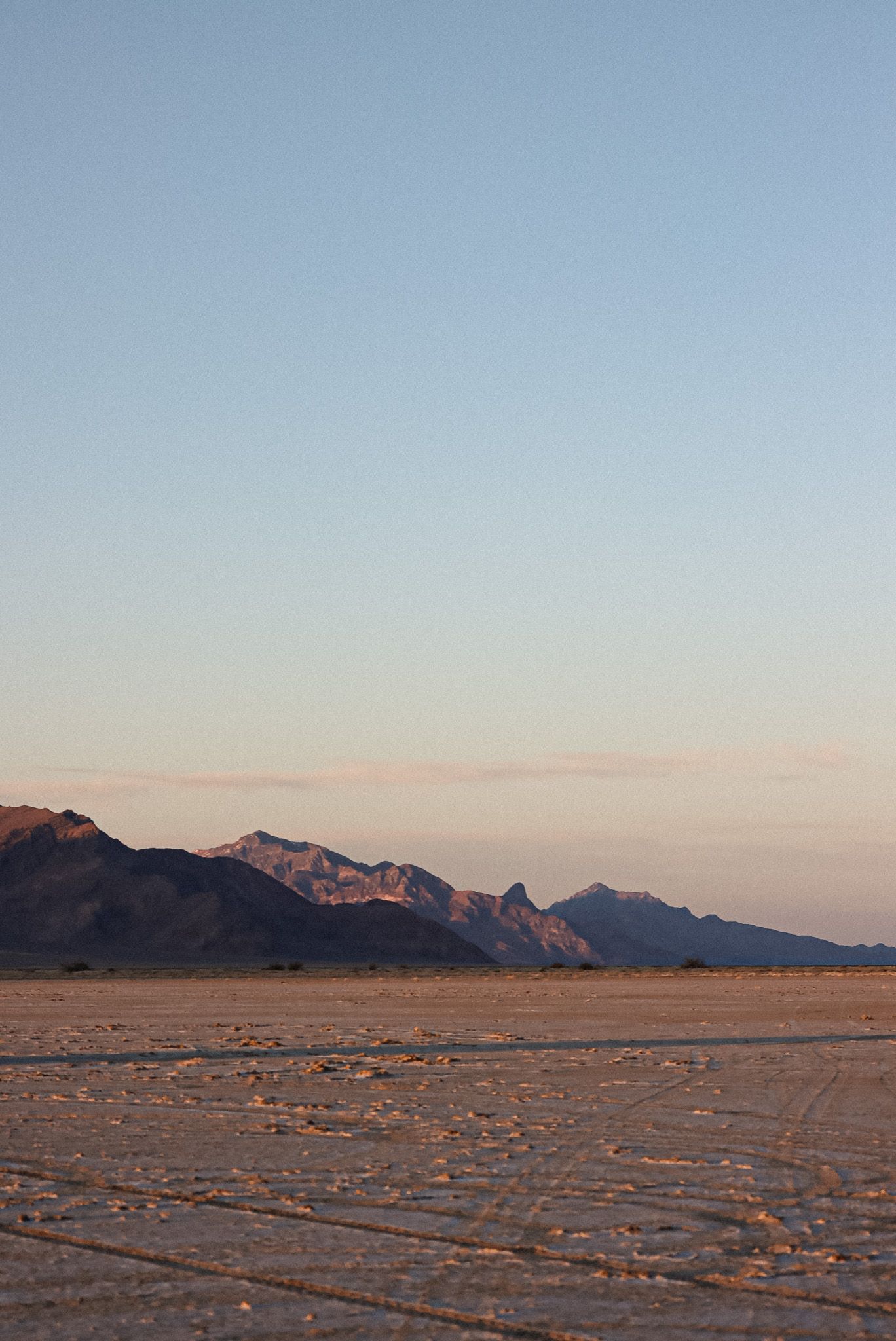 Cora Emilie Media Desert landscape at sunset with rugged mountain silhouettes against a pale sky.