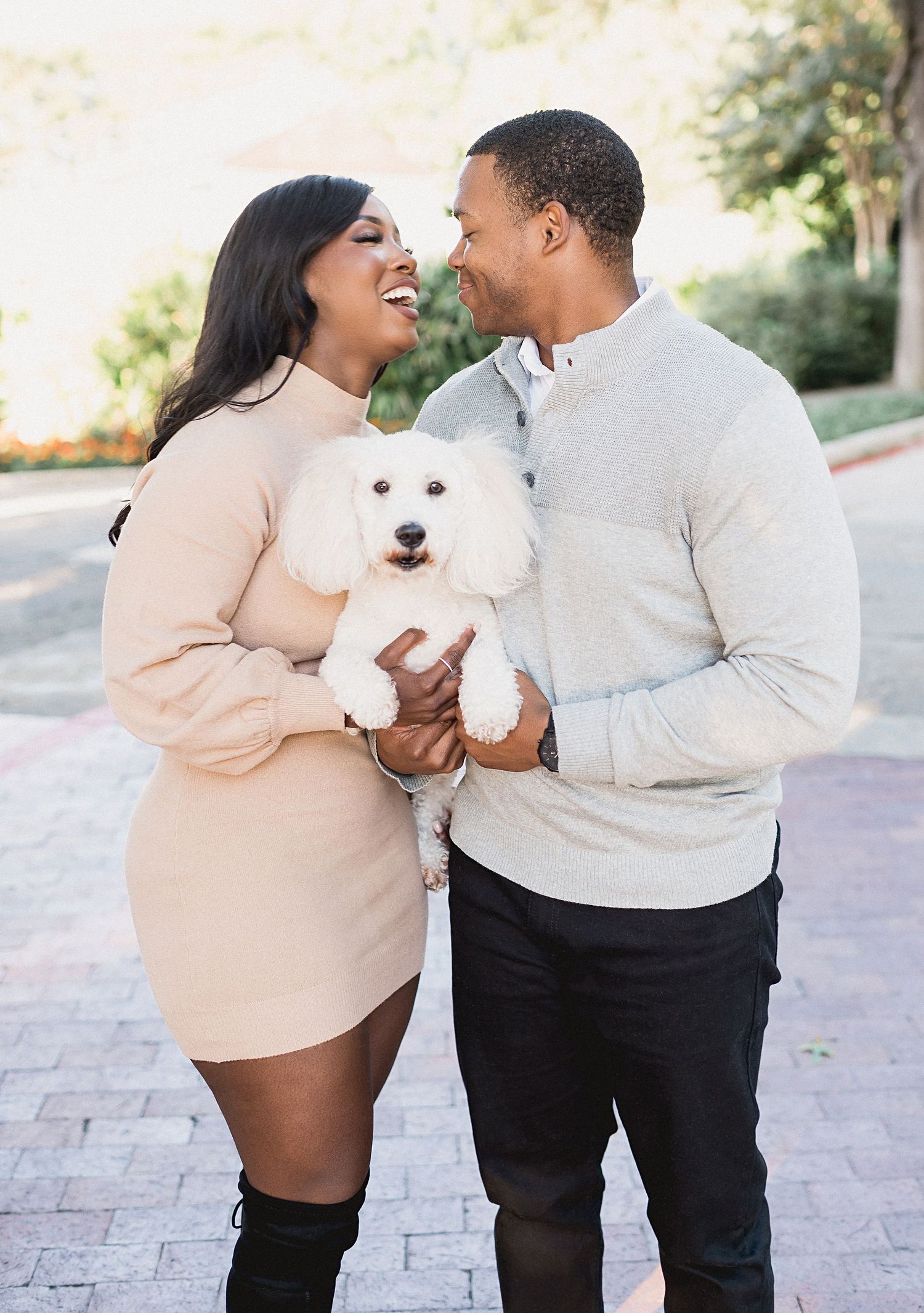 Couple sharing a joyful moment while holding their small white fluffy dog.