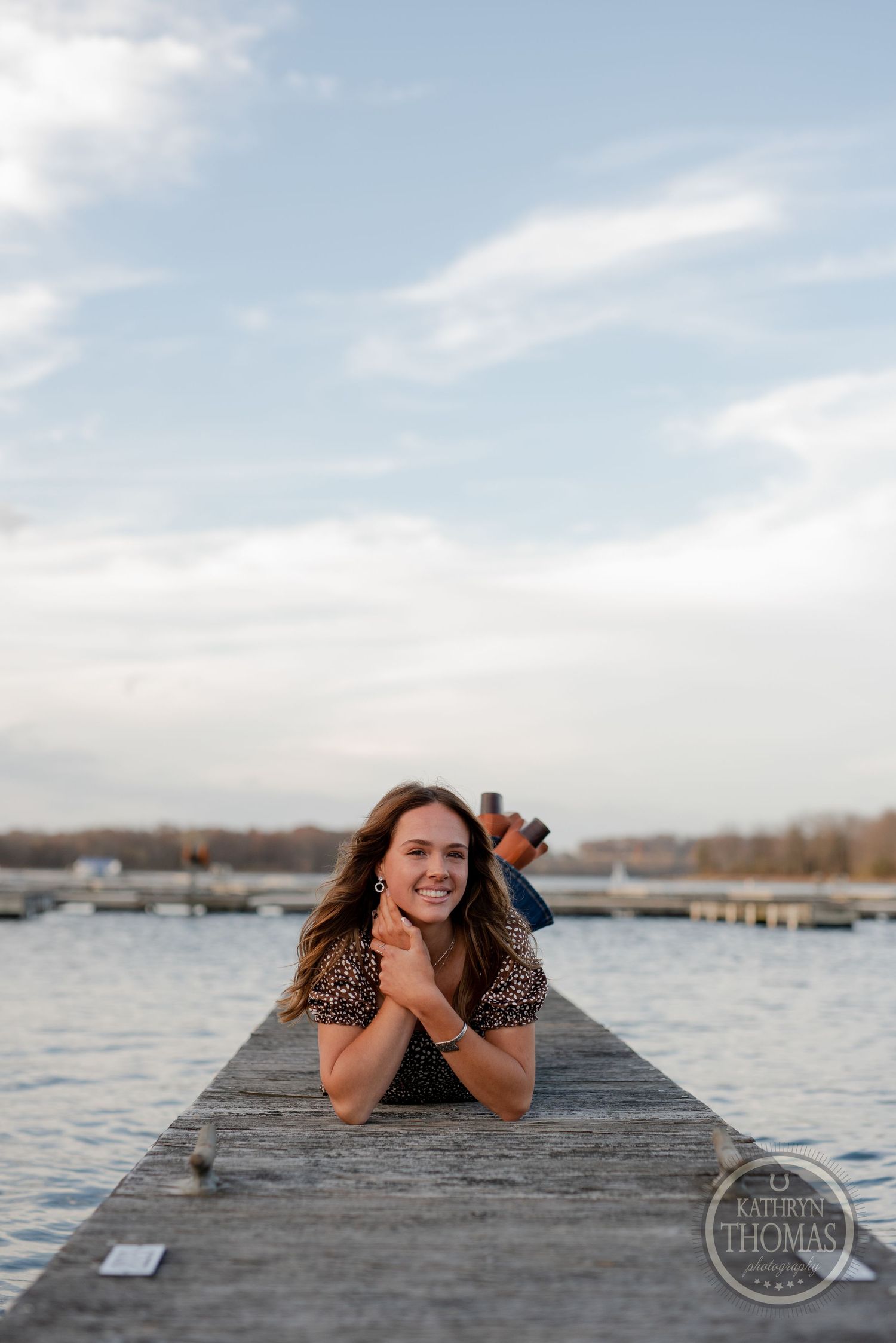 Someone lying on a wooden pier overlooking a lake with boats and docks in the distance.