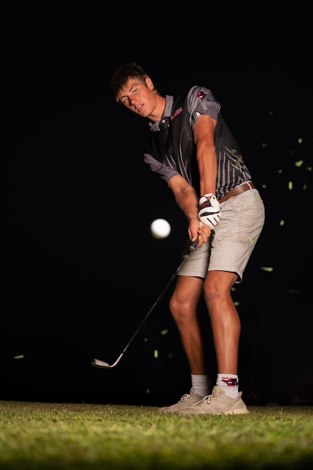 Golfer practicing chip shots at night under stadium lights.
