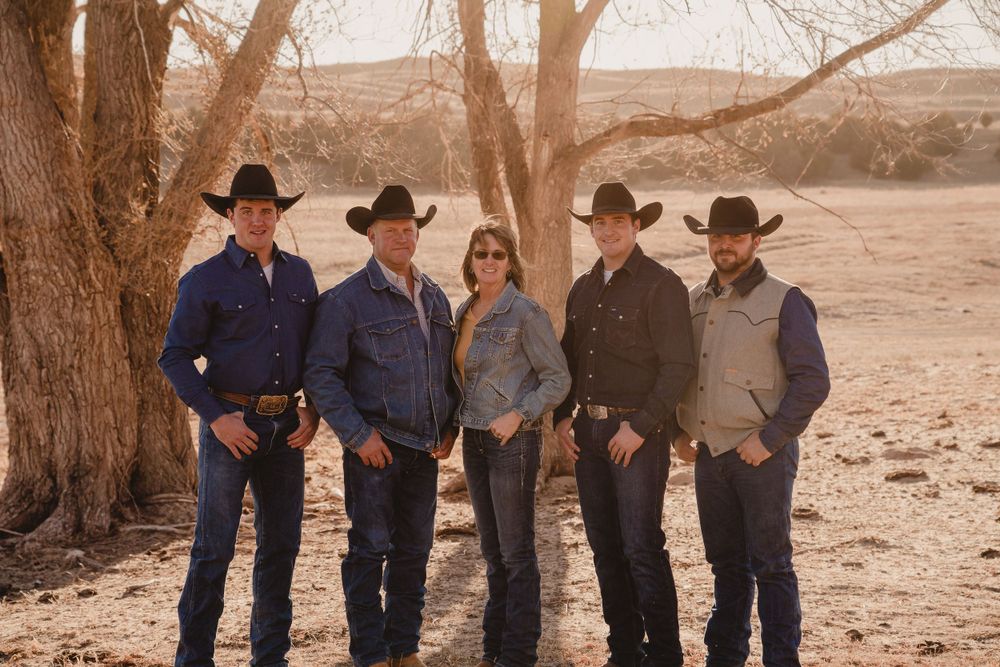 A group photo of people in cowboy hats and western attire standing together outdoors.