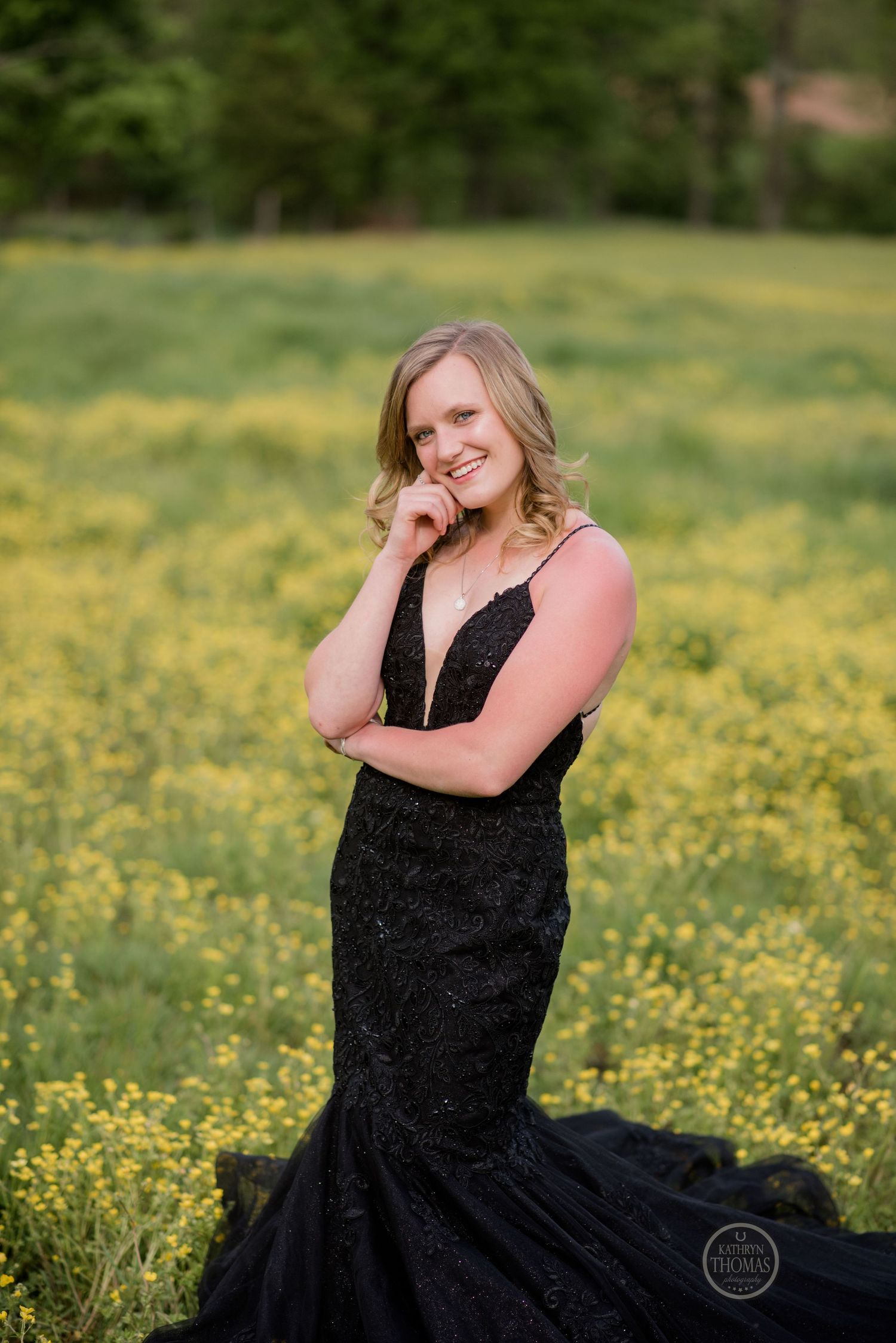 A figure in a black mermaid-style gown poses confidently in a field of yellow spring flowers.