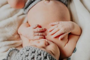 Close-up shot of baby's hands and belly with knitted gray fabric.