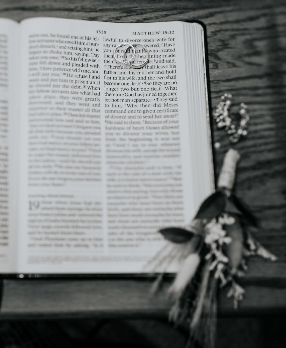 Black and white photo of open Bible with dried flowers on wooden surface.