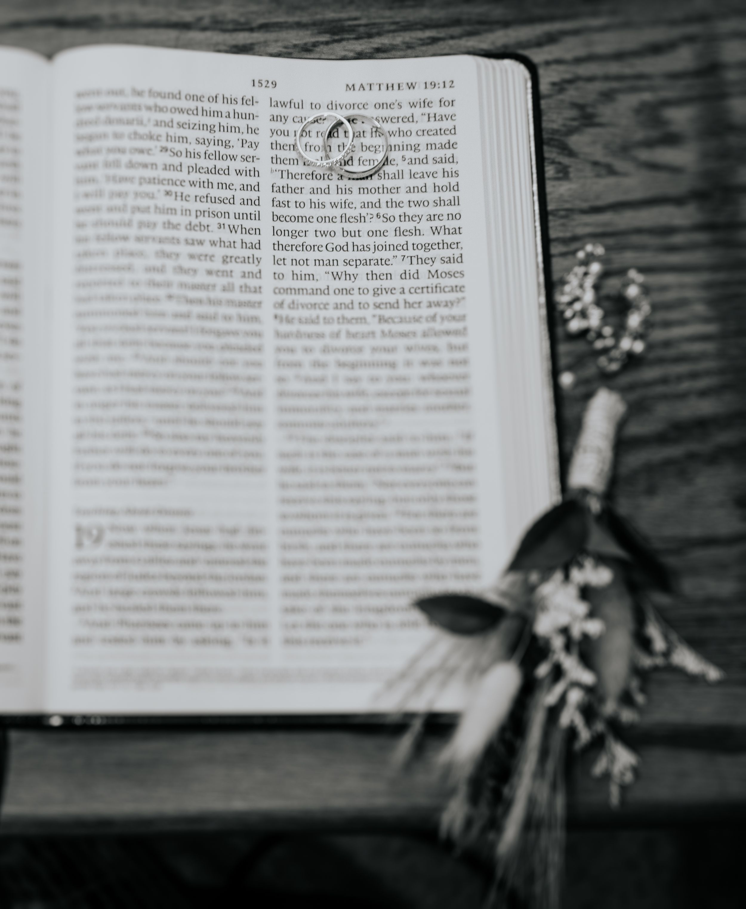 Black and white photo of open Bible with dried flowers on wooden surface.