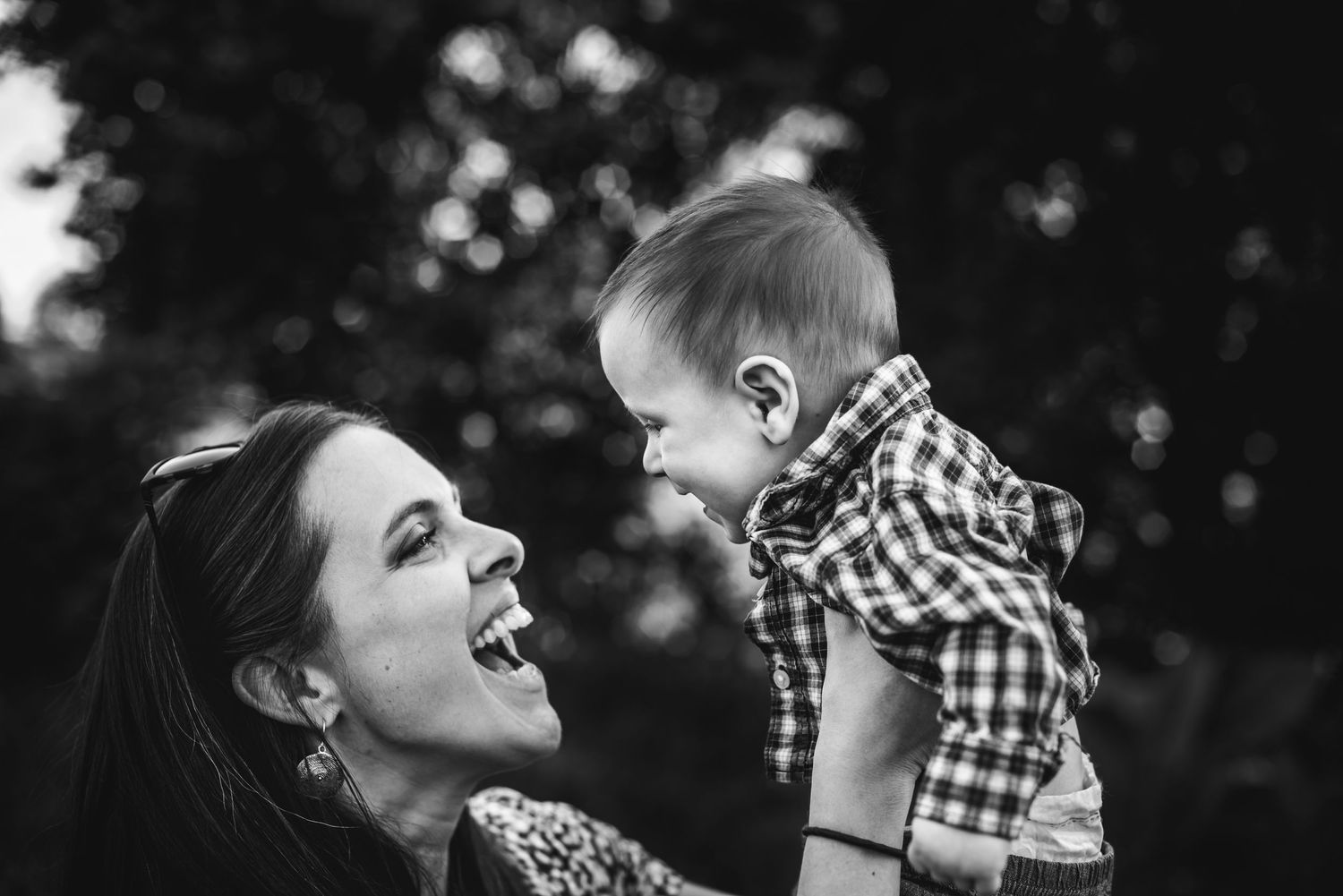 BW image of a smiling woman as she holds up her baby son and he smiles back at her.