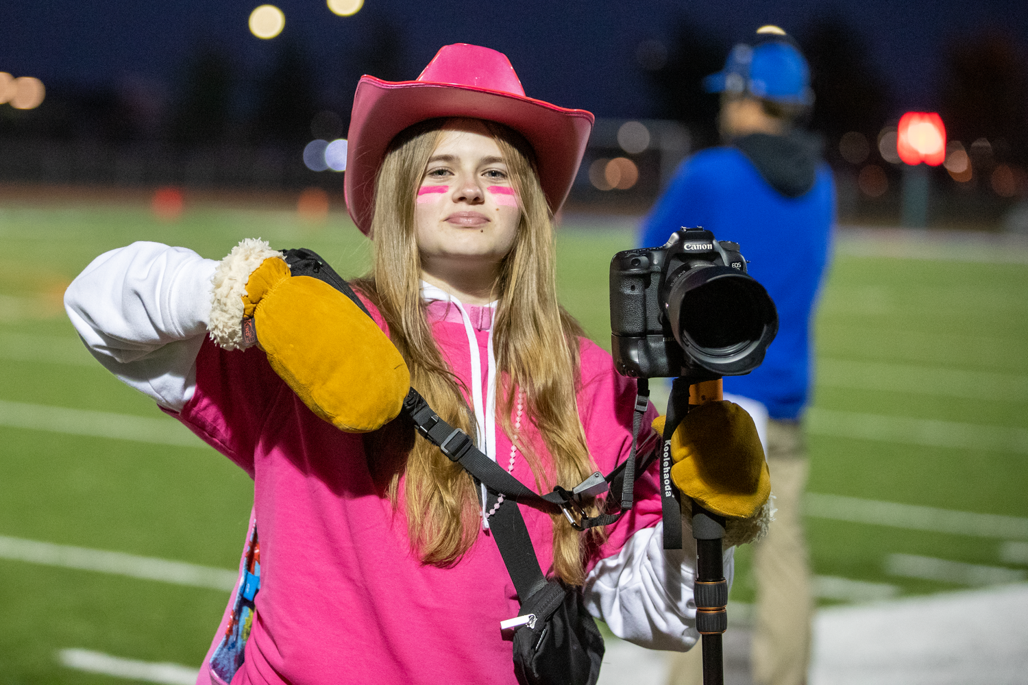 Sports photographers in pink shirts capture action shots on a football field at night.