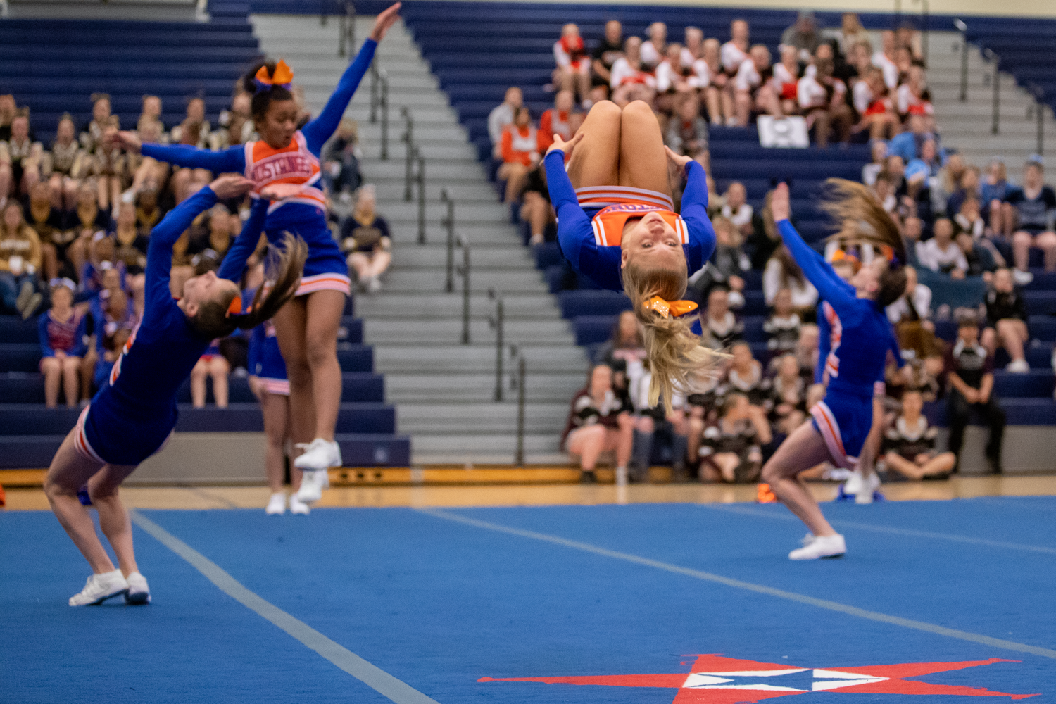 Cheerleaders perform dynamic routines and stunts on a blue competition mat.