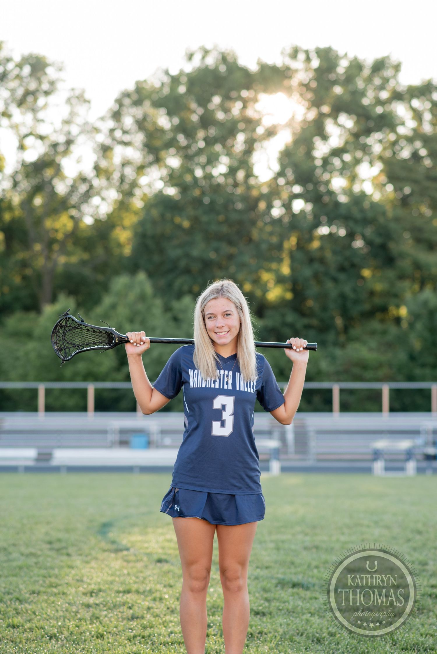 Lacrosse player in Manchester Valley uniform #3 poses on sports field at sunset.