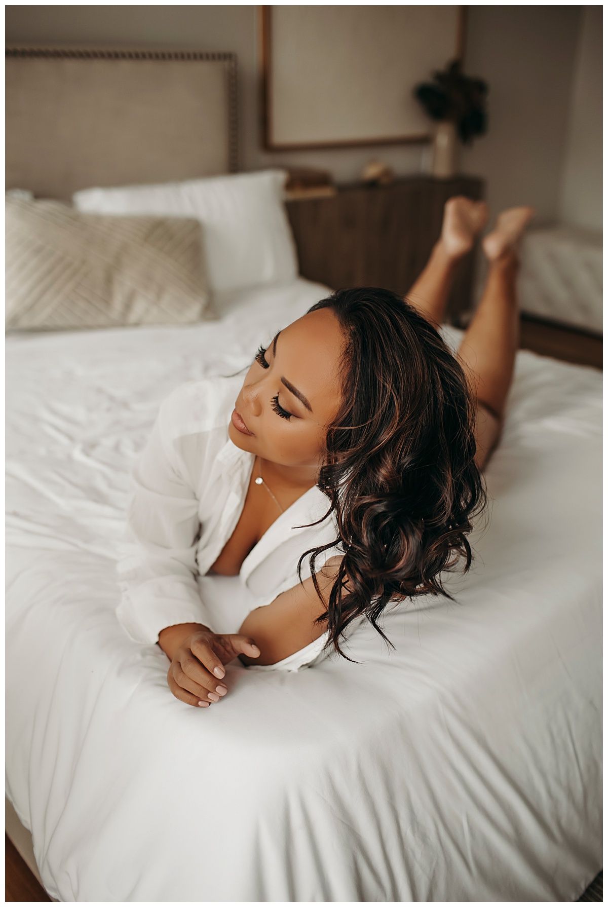 woman wears a white shirt while laying on the bed during empowering boudoir session