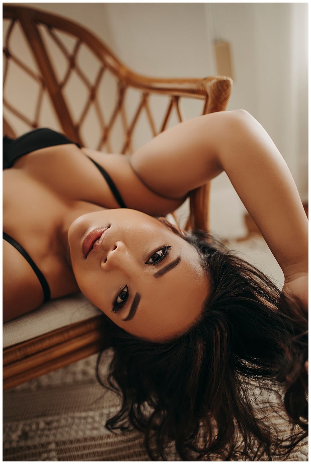 woman runs hands through hair laying on a chair during empowering boudoir session