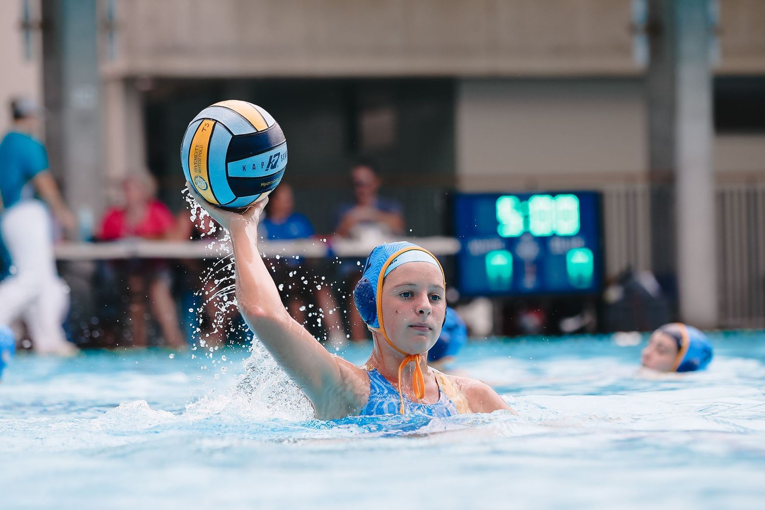 Water polo player raising blue ball above water during match.
