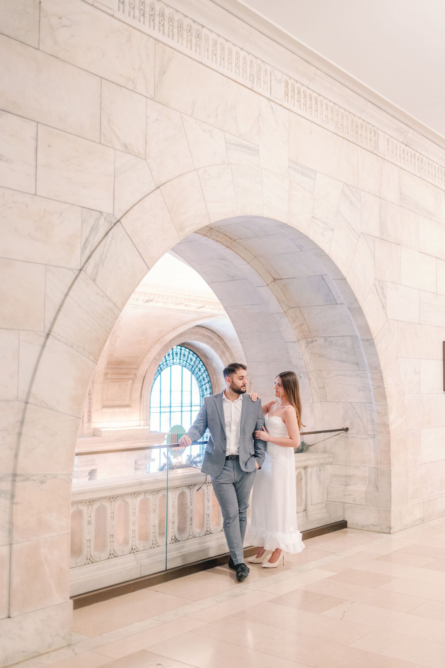 Couple in wedding attire standing under marble arch at New York Public Library.