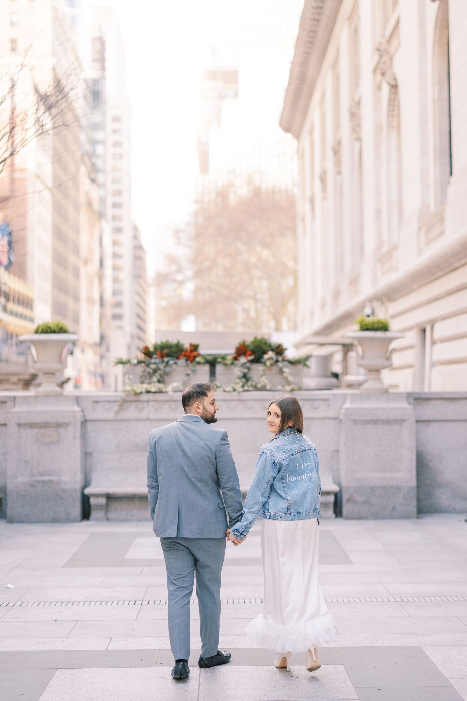 Newlyweds holding hands outside New York Public Library in city setting.