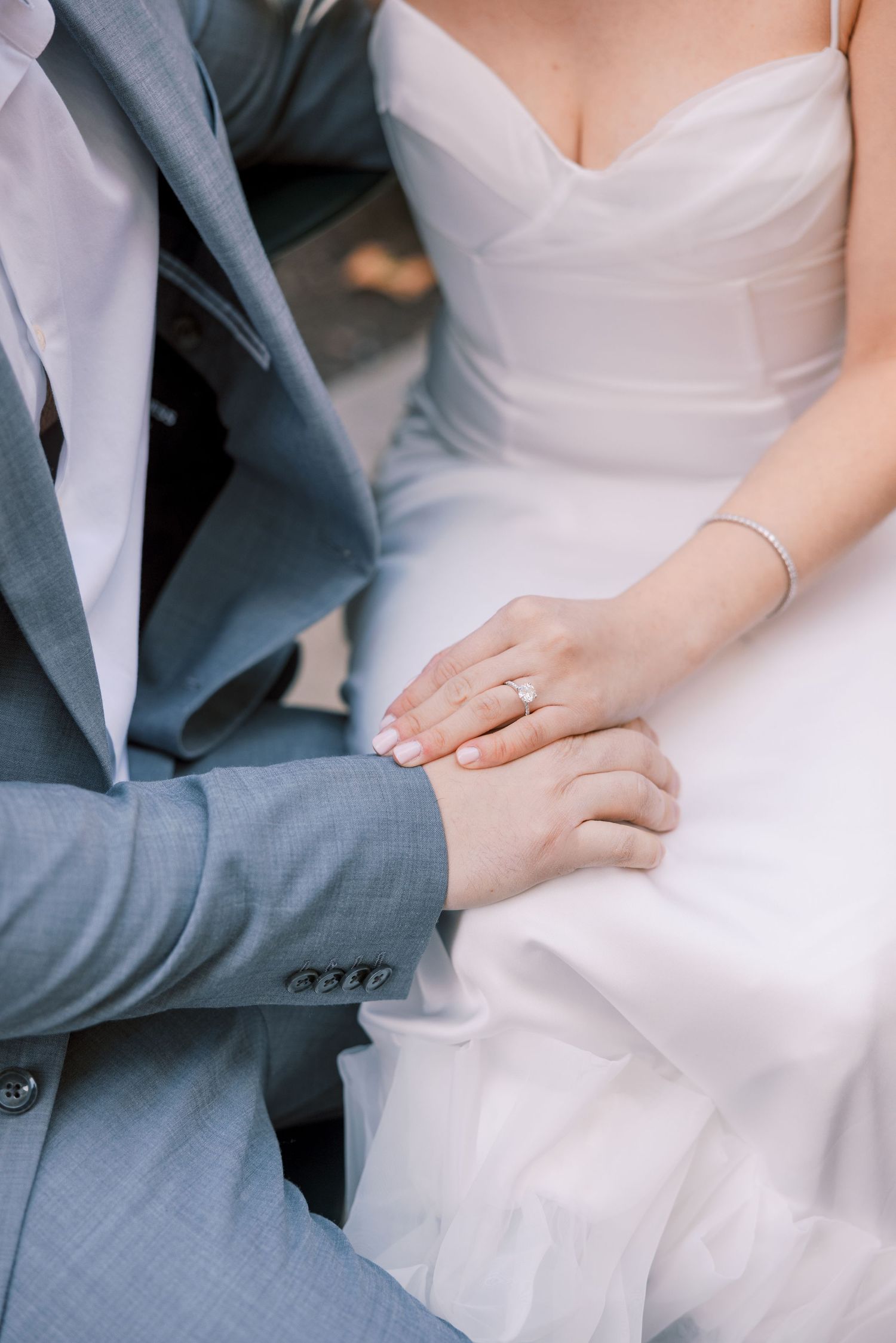 Close-up of couple holding hands showing diamond engagement ring, bride in white gown.