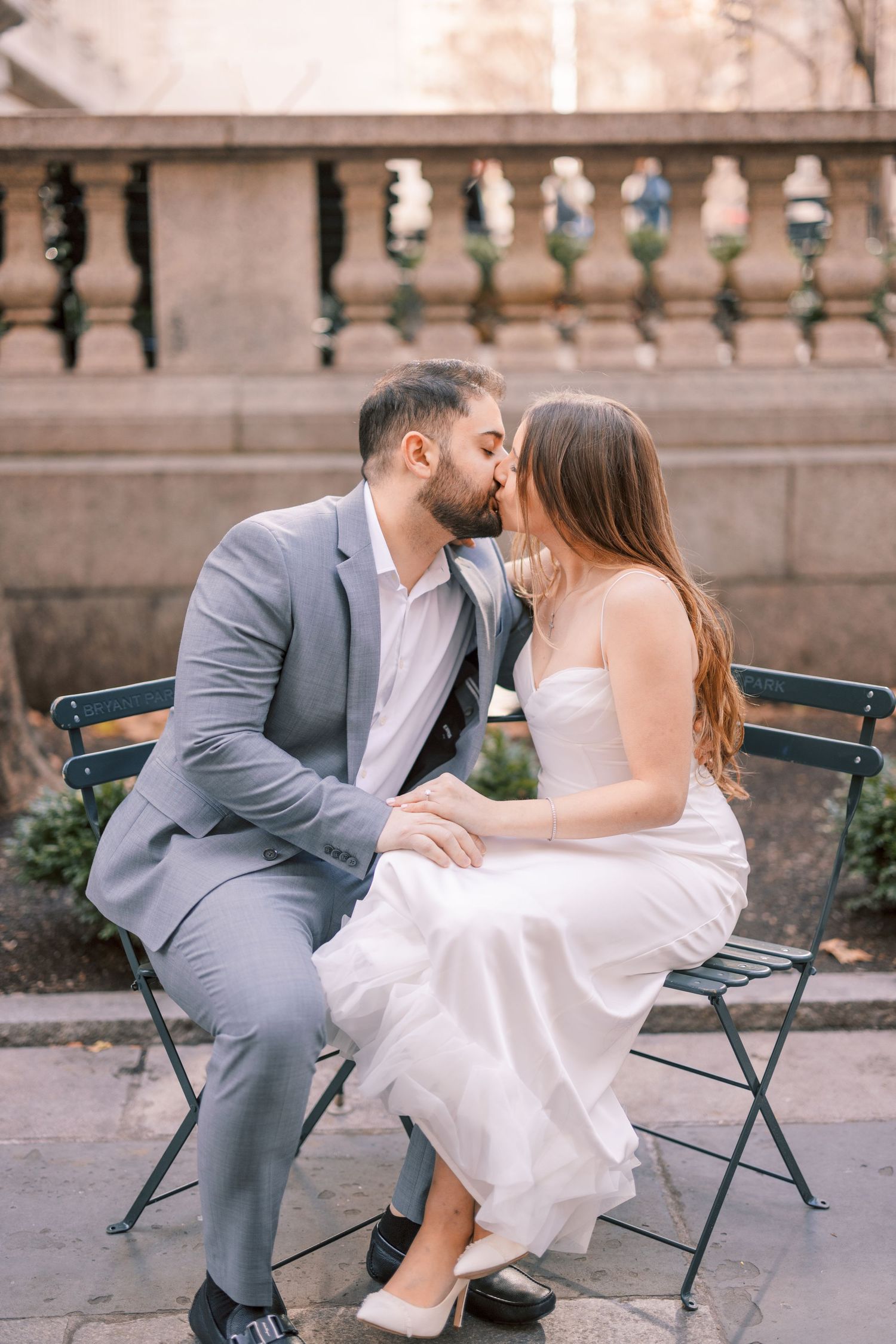 Bride and groom sharing a kiss while seated on outdoor bench.