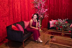 Elegant scene with woman in red dress seated on dark couch with floral arrangements.