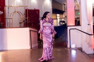 Woman in flowing pink satin gown walks gracefully through elegant venue with pillars.