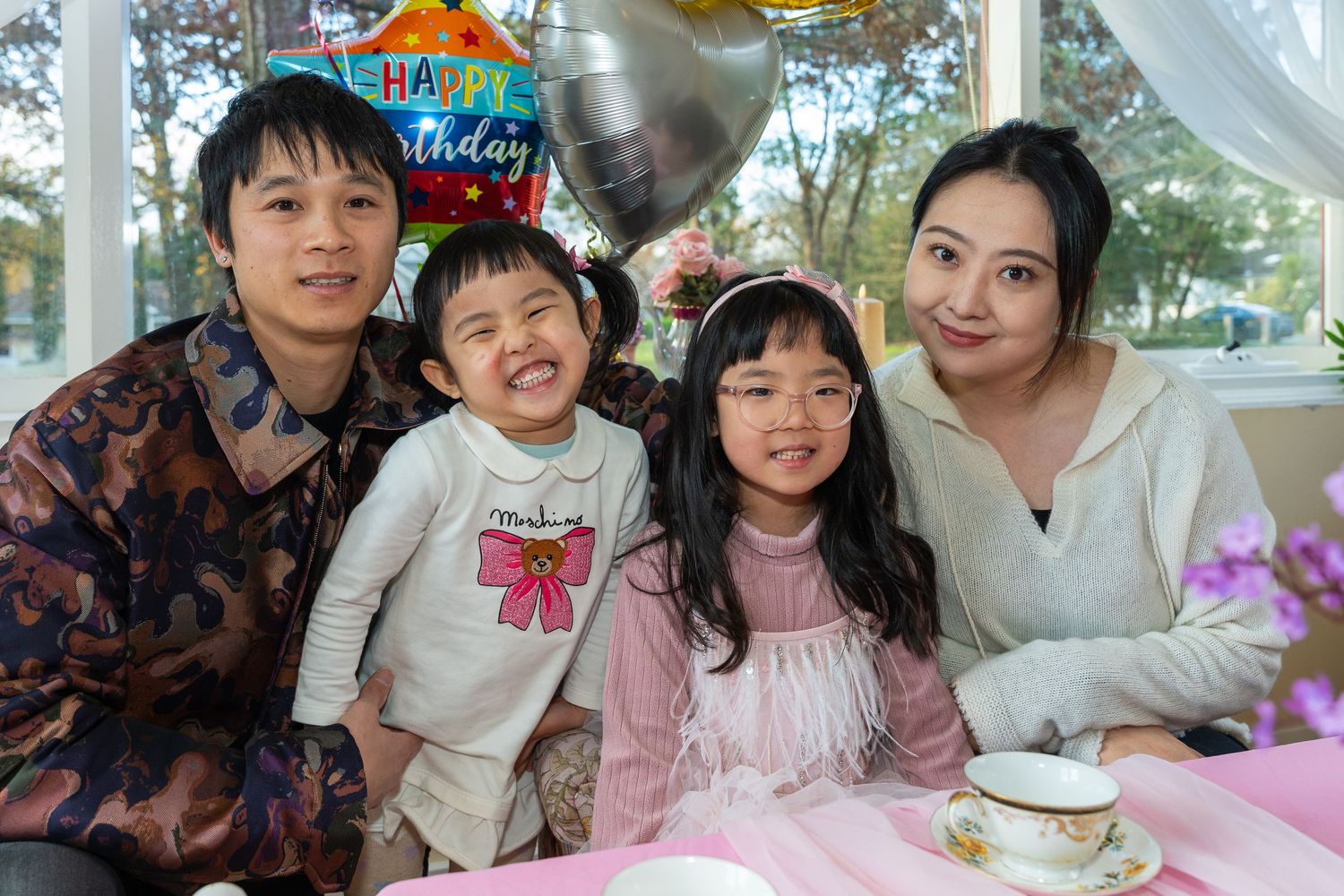 Asian family of four celebrating birthday with happy balloon at a colorful indoor tea party.