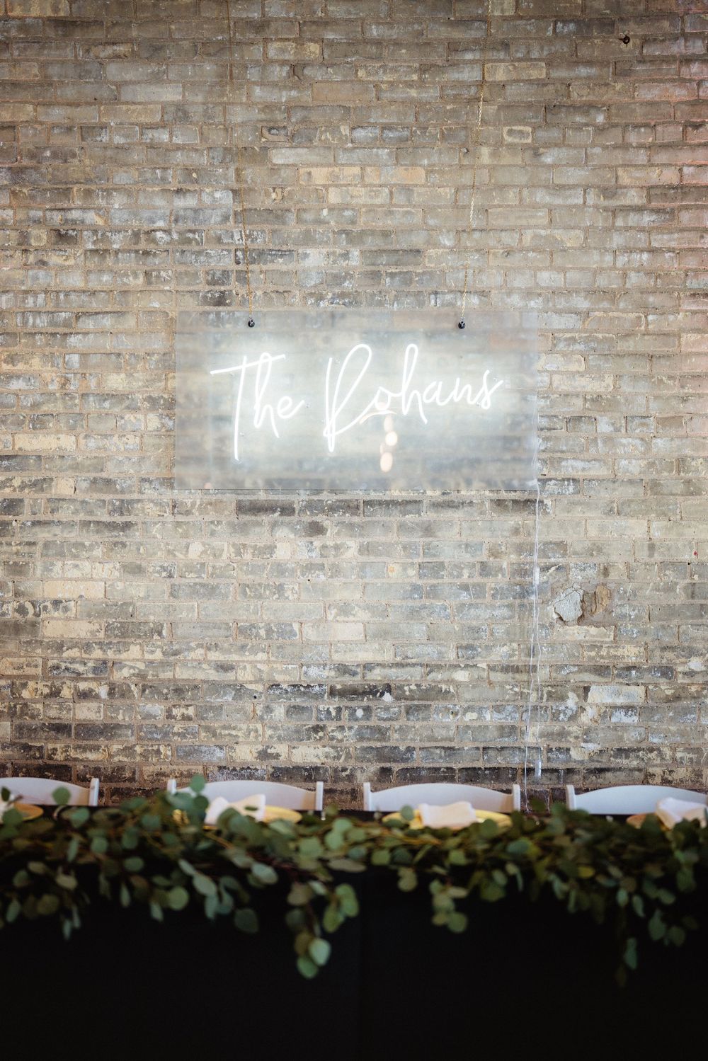 A glowing neon sign reading 'The Balance' mounted on an exposed brick wall with greenery below.
