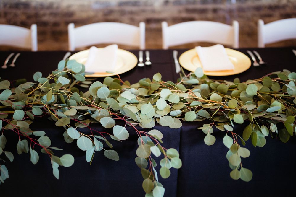 Table setting with black tablecloth decorated with eucalyptus garland and white place settings.