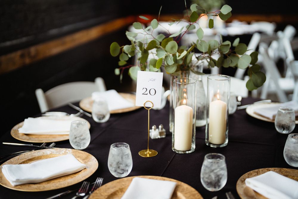 Elegant table setting with gold chargers, white napkins and floral centerpiece with table number twenty.