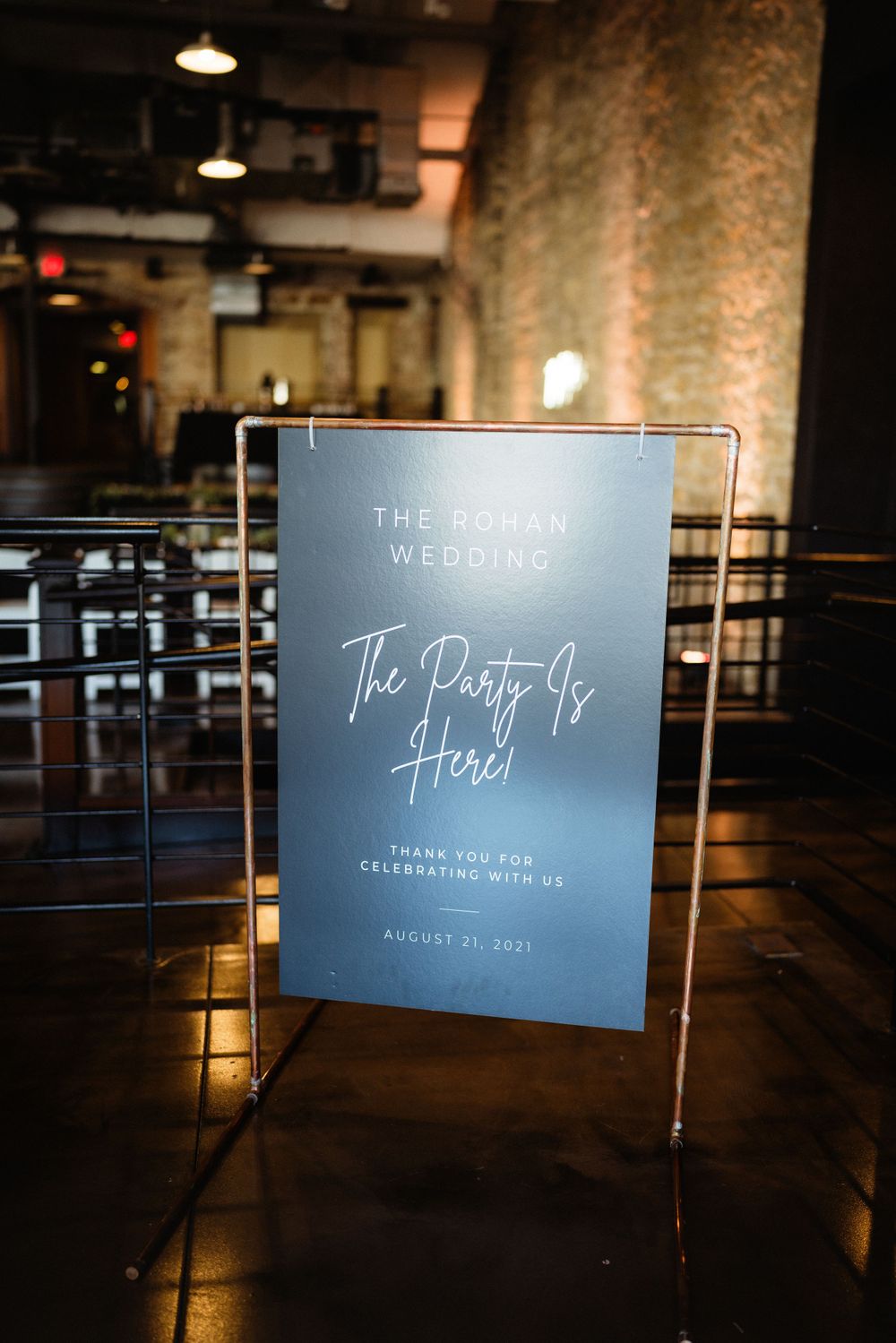 Wedding welcome sign in clear frame reading 'The Party Is Here' at an industrial venue.