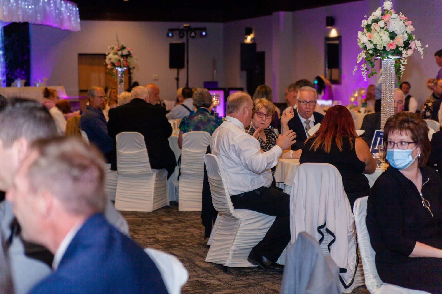 Wedding reception guests dancing and mingling in an elegantly decorated venue with white chairs.