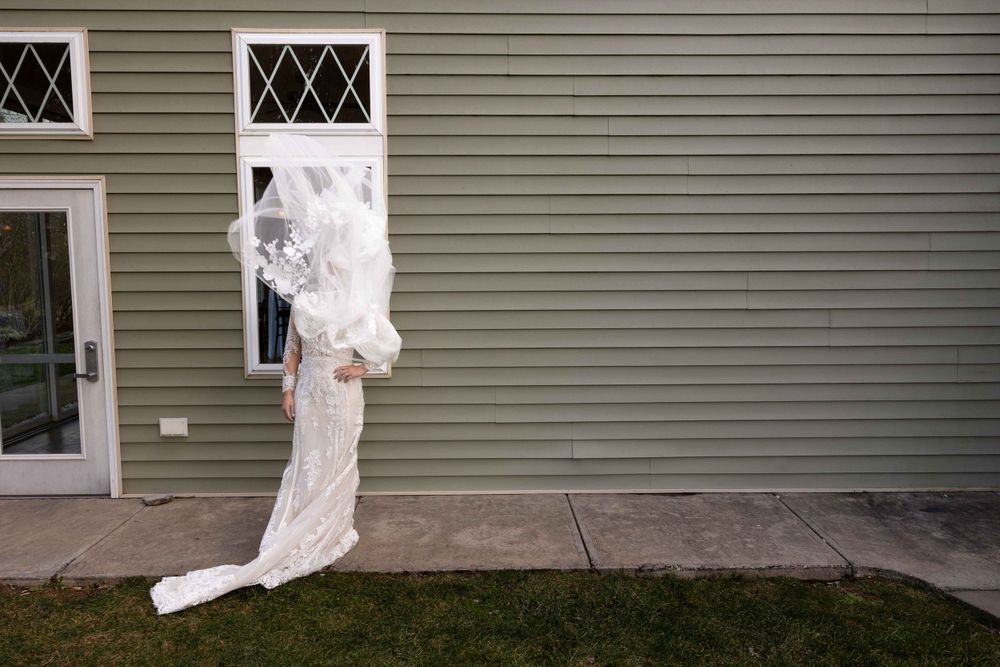 Elegant white wedding dress hanging outside a gray building with diamond-paned windows.