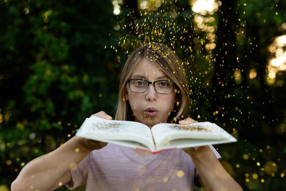 Glitter falls while someone blows across an open book in an artistic outdoor photo.