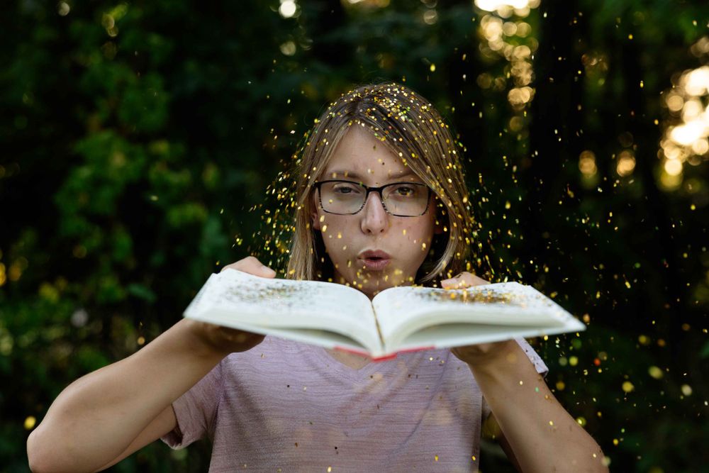 Sparkles scatter as someone blows across pages of an open book at sunset.