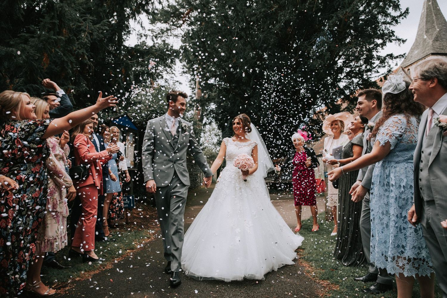 A bride and groom walk hand in hand while guests throw confetti. The joy is beautifully captured by a wedding photographer in Basildon Essex