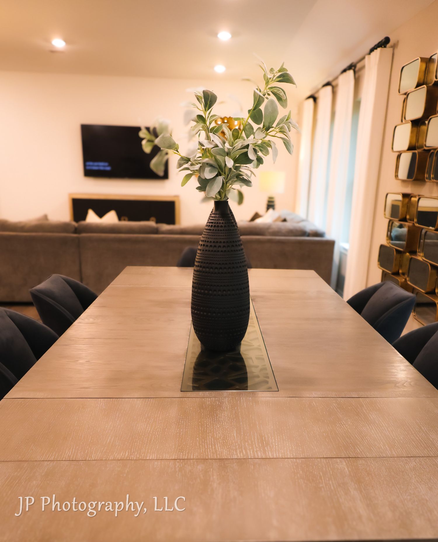Modern dining table with black textured vase and green foliage centerpiece.
