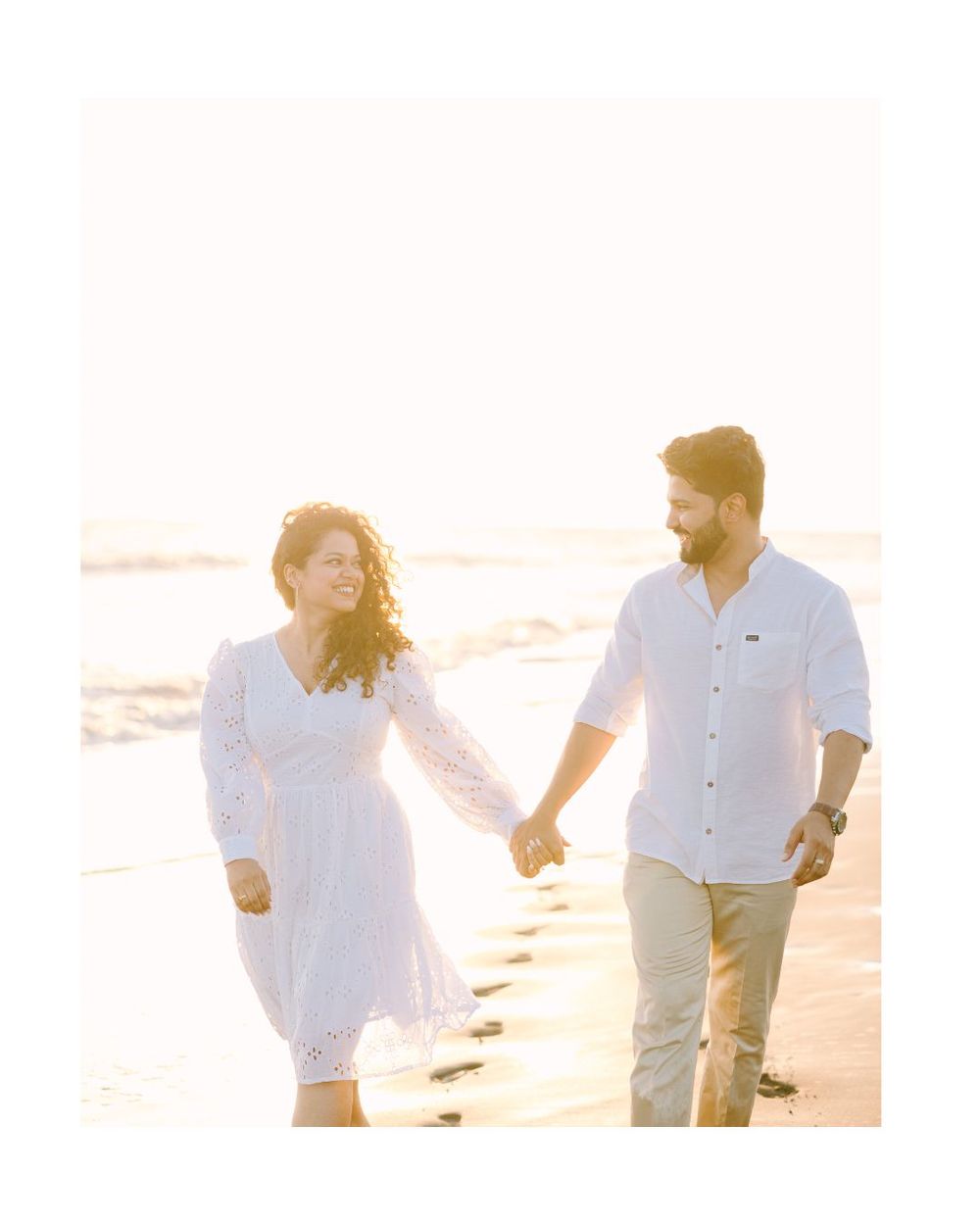 Couple walking and laughing together on sandy beach during golden hour.