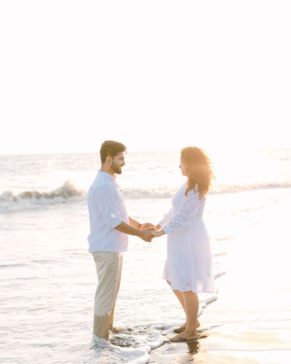 Beach proposal scene with couple standing in shallow ocean water at sunset.