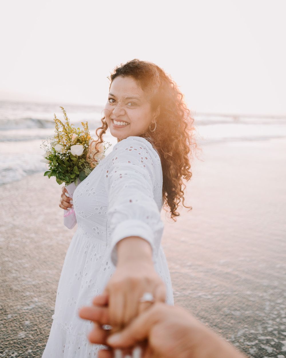 Follow-me style photos of couple holding hands on beach at sunset.