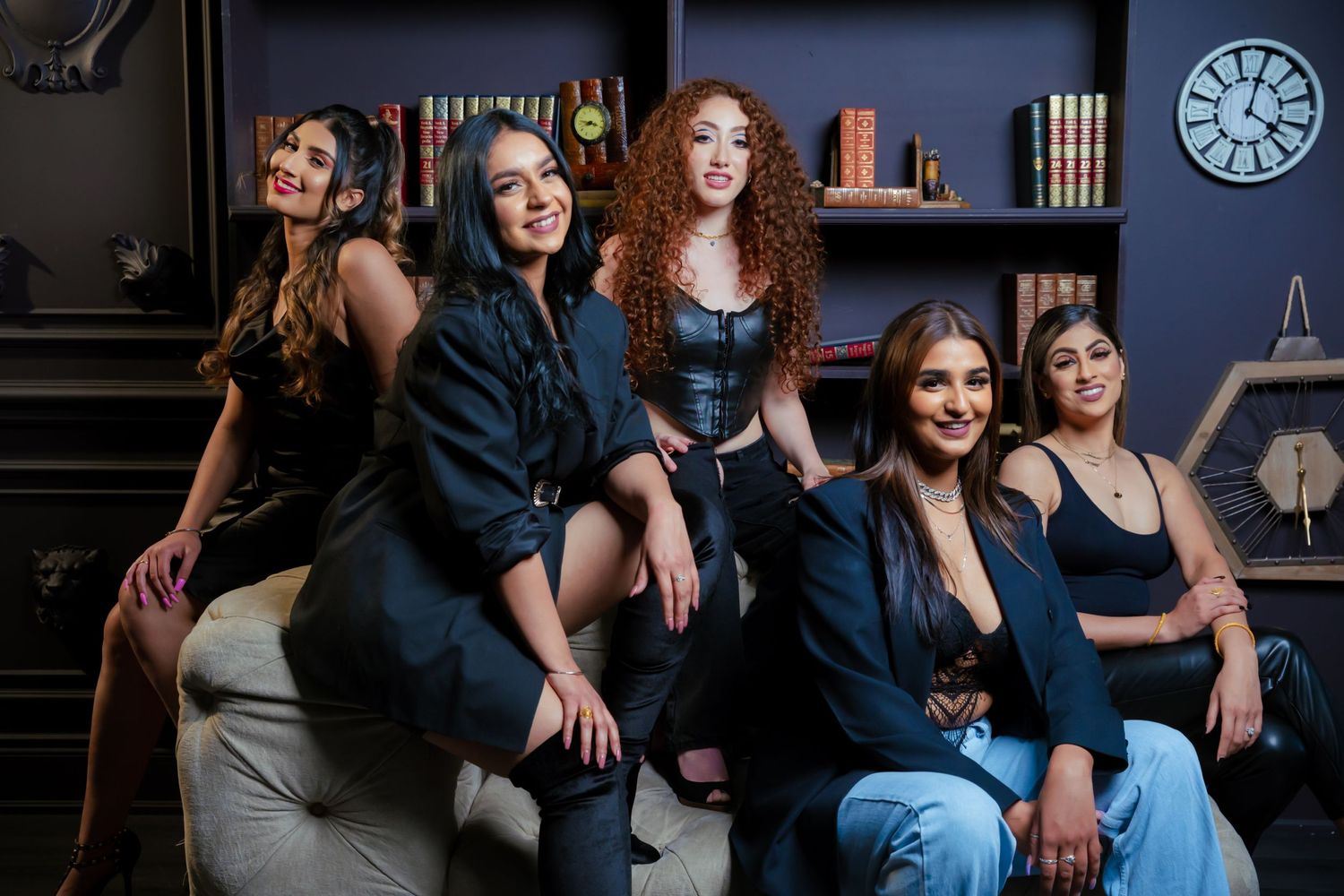 Group portrait of five friends in casual and dressy attire posed in library setting.