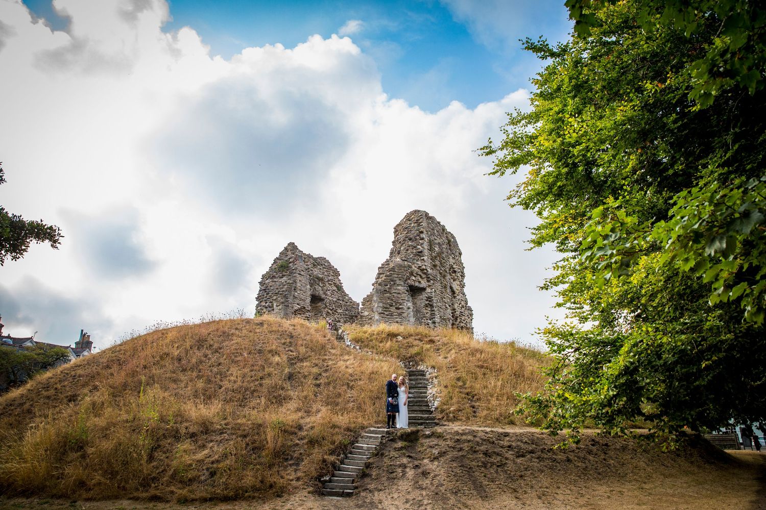 Panoramic view of castle ruins on hilltop against blue sky with clouds.