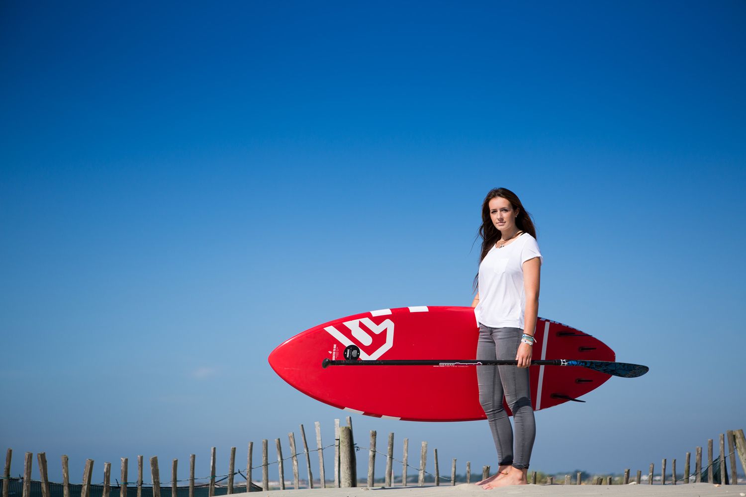 Person holding red surfboard on sandy beach with blue sky background during business branding photoshoot.