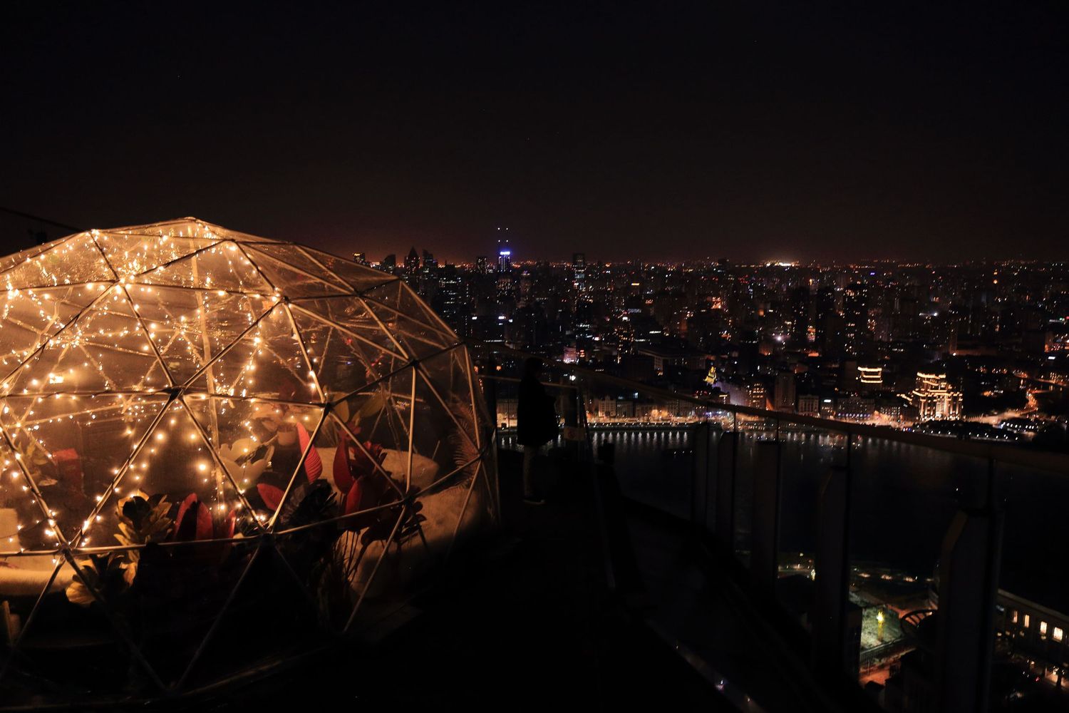 Illuminated dome-shaped structure overlooking city lights at night.
