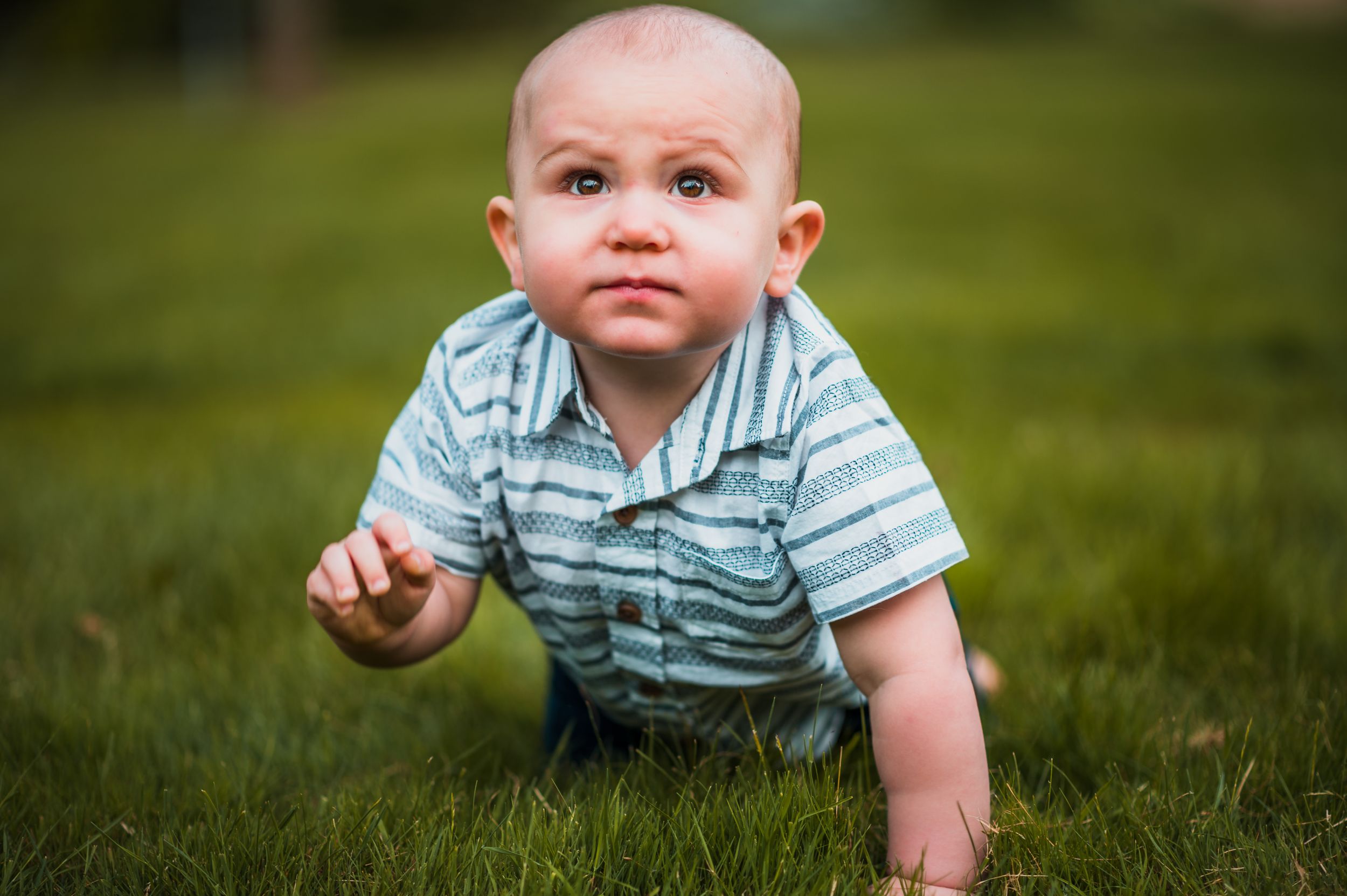 Baby in striped outfit crawling on grass during outdoor photo session.