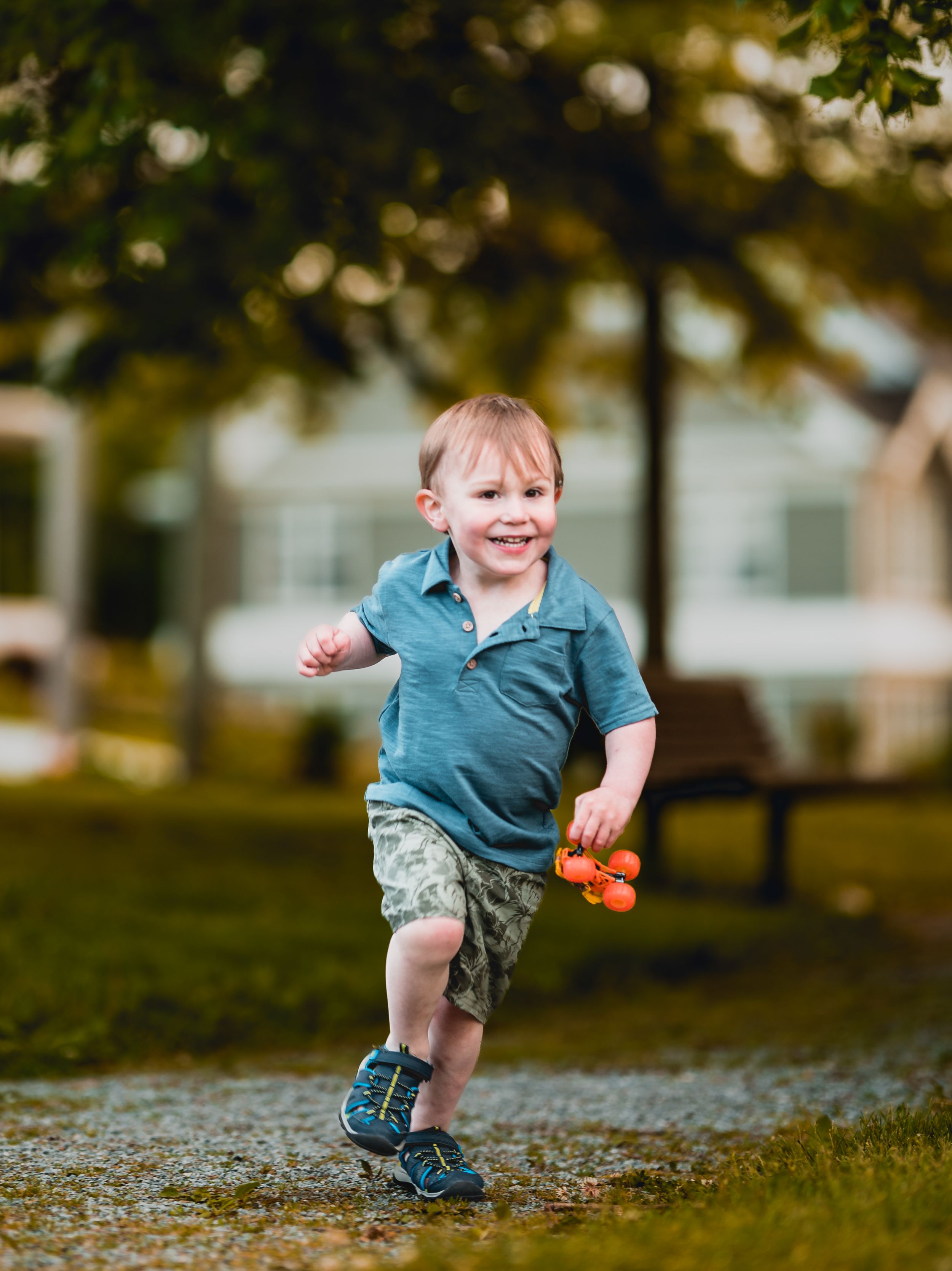 Small child running and playing on gravel path under trees in park.