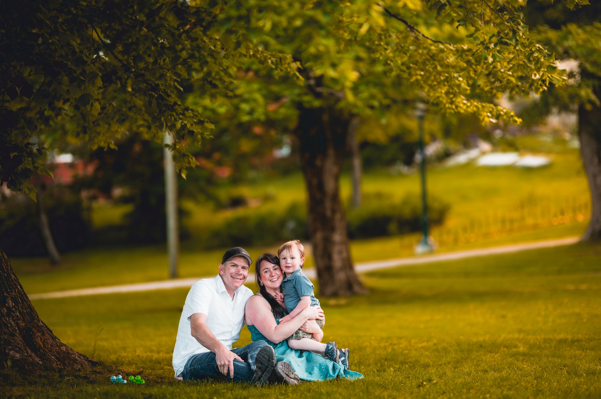 Family relaxing together on blanket under trees in park setting.