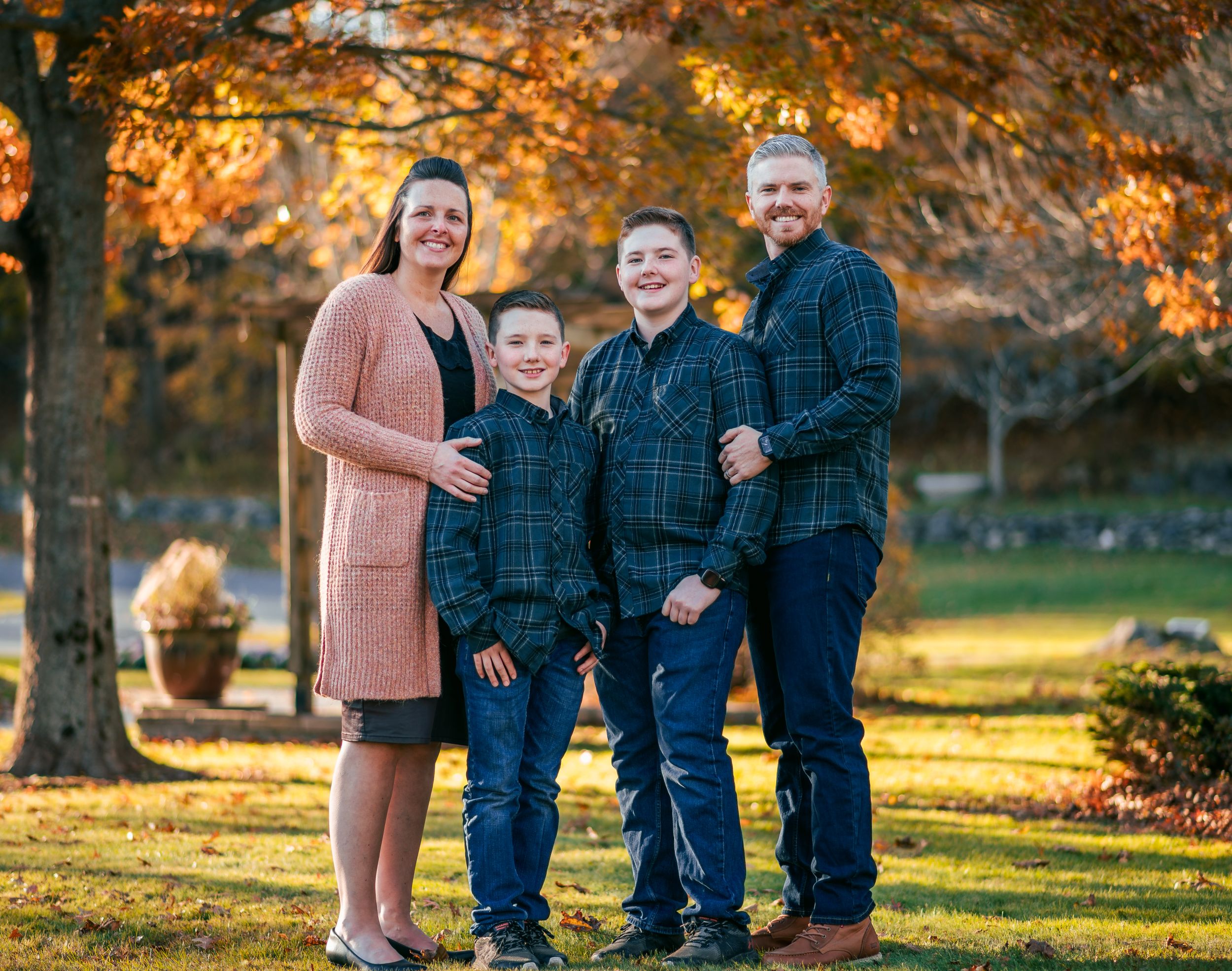 Family members sitting together on grass during golden hour with fall foliage in the background.