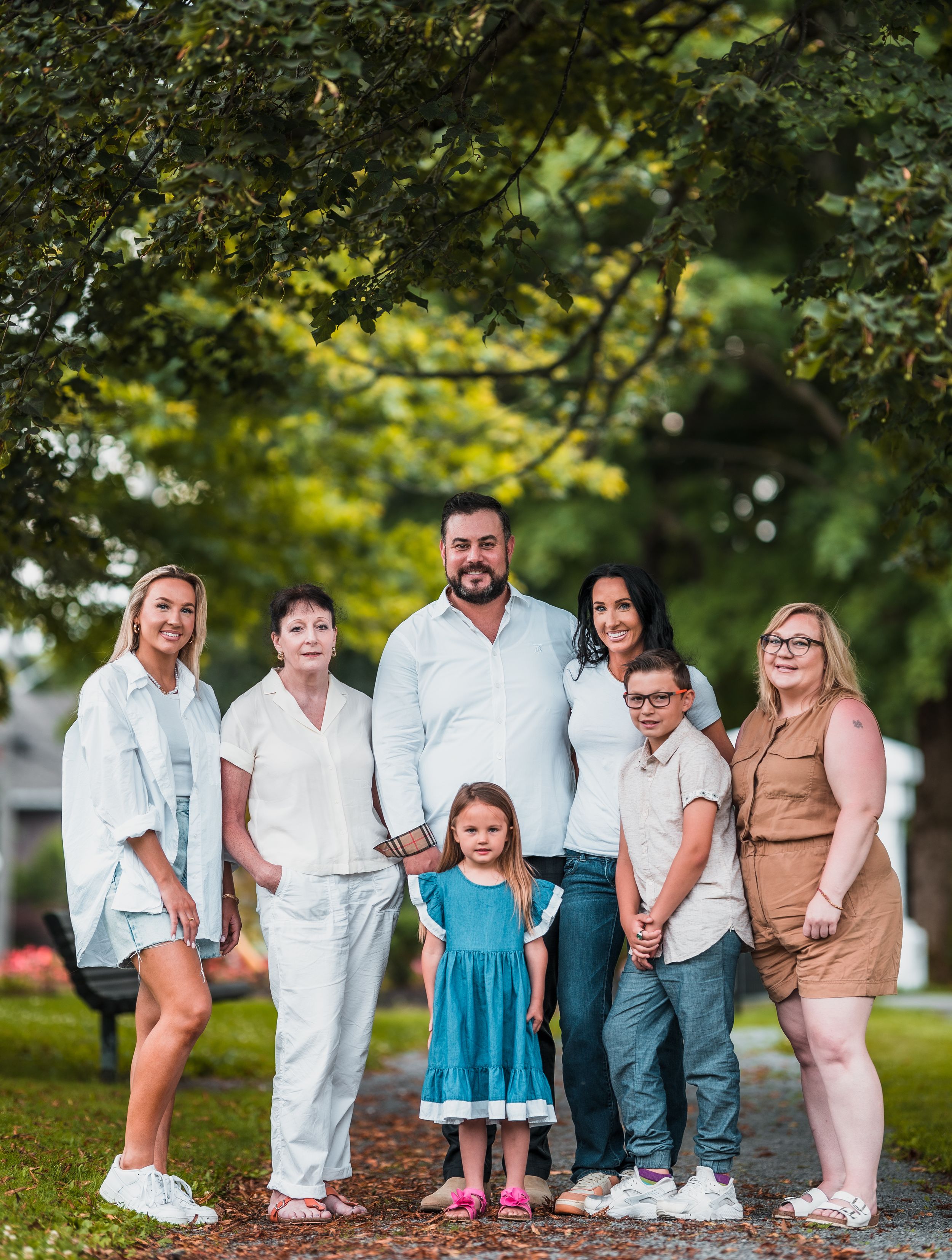 Extended family group portrait under trees wearing coordinated white and neutral outfits.