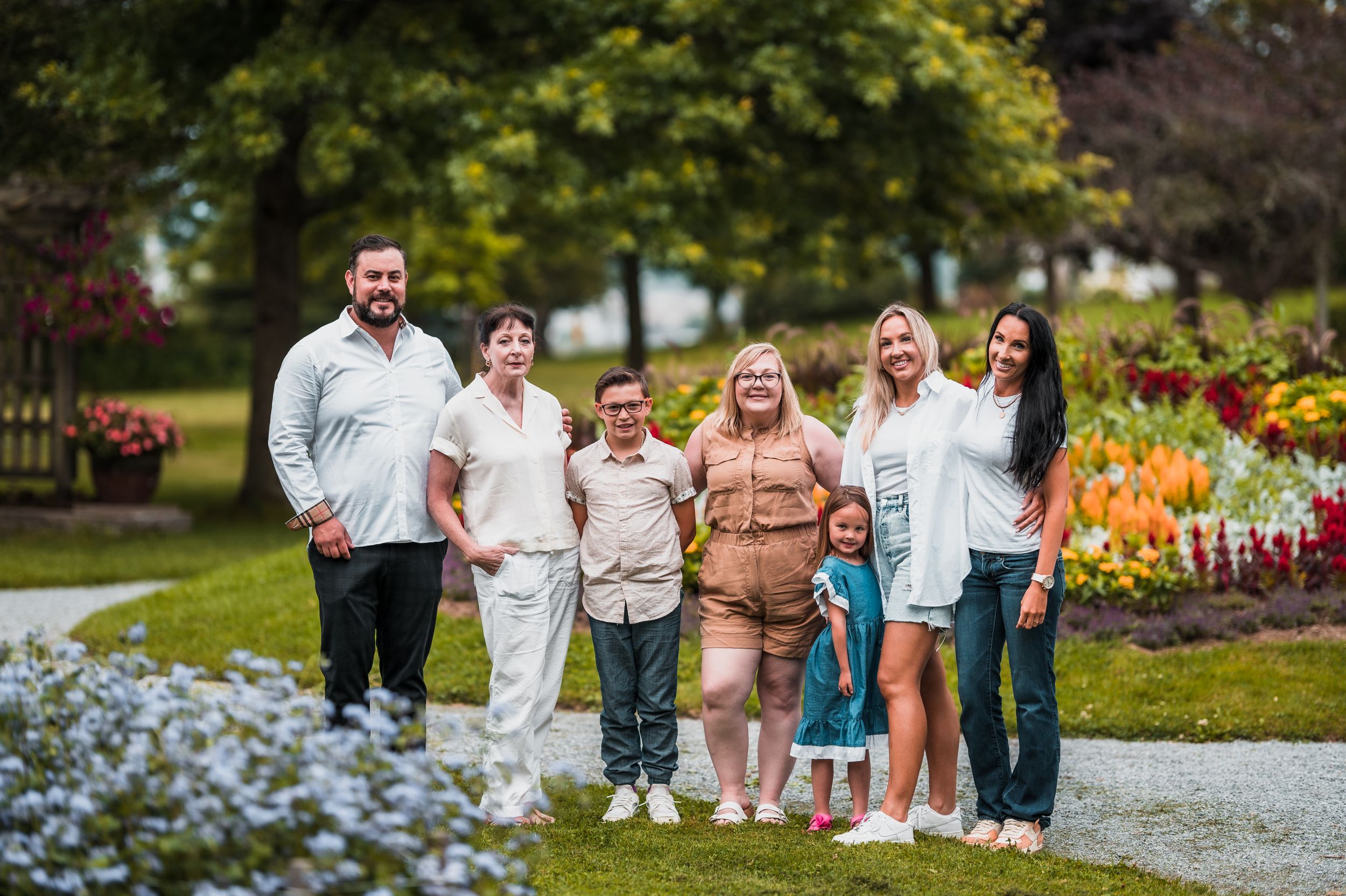 Large family group posing together outdoors with flowers and greenery in background.
