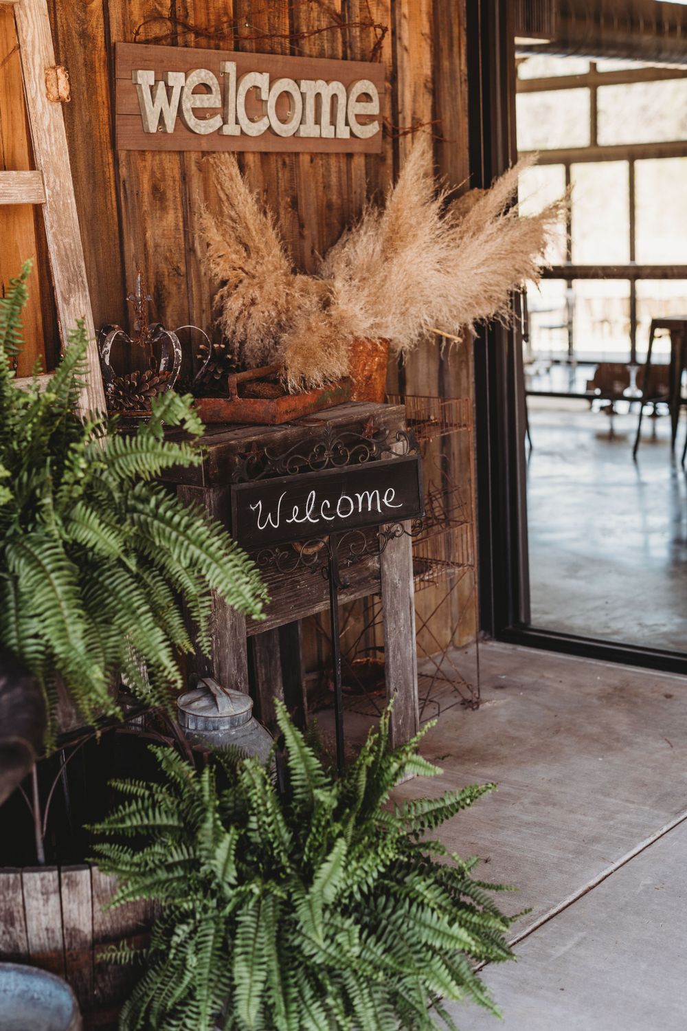 Rustic welcome sign with ferns and pampas grass decorating a wooden entrance.