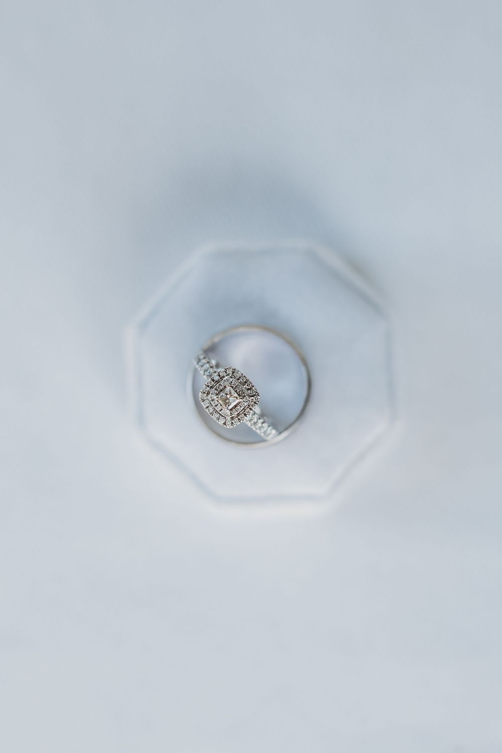 A diamond engagement ring displayed on a white octagonal surface.